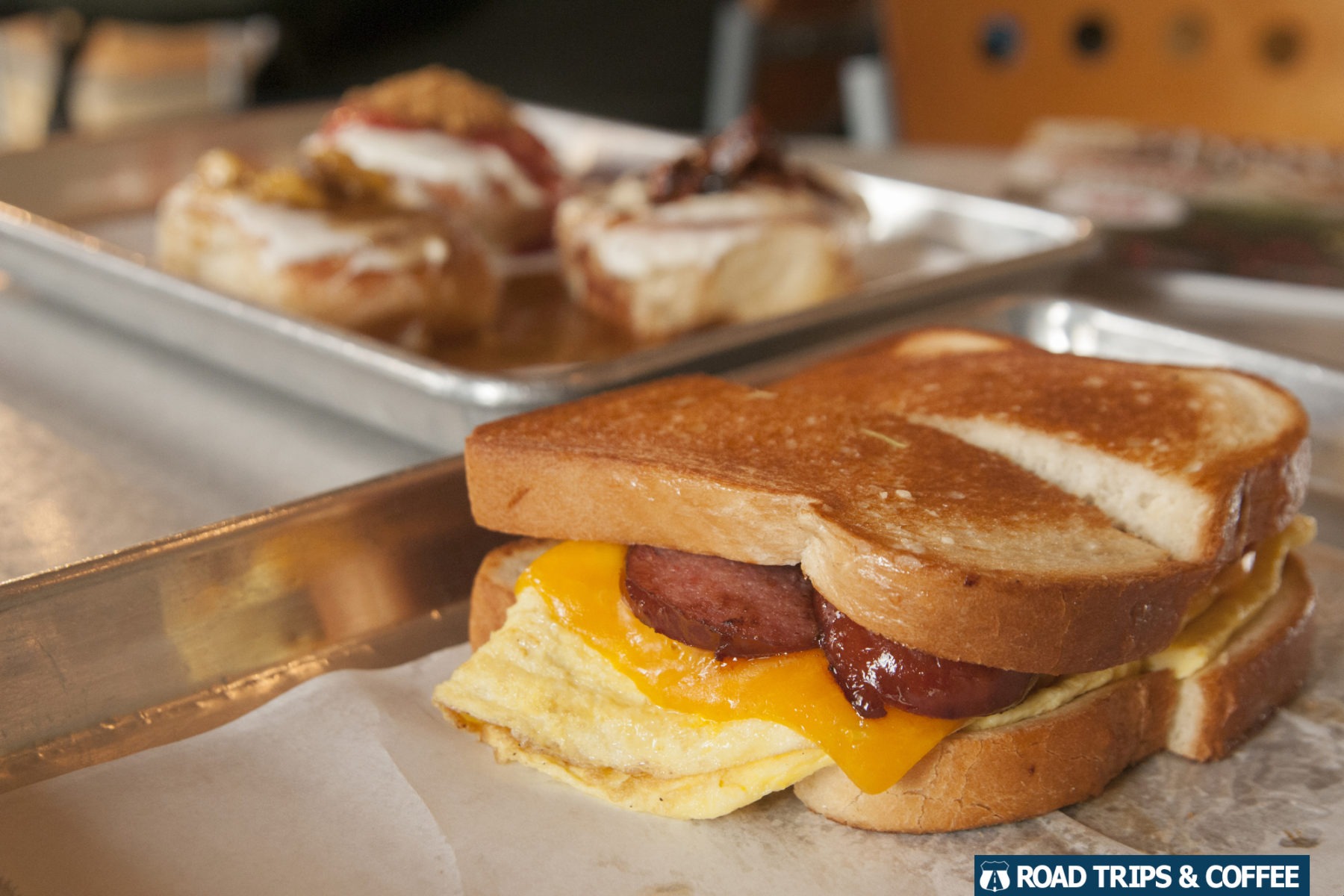 A smoked sausage breakfast sandwich on a shiny metal tray at The Devine Cinnamon Roll Deli during brunch in Columbia, SC