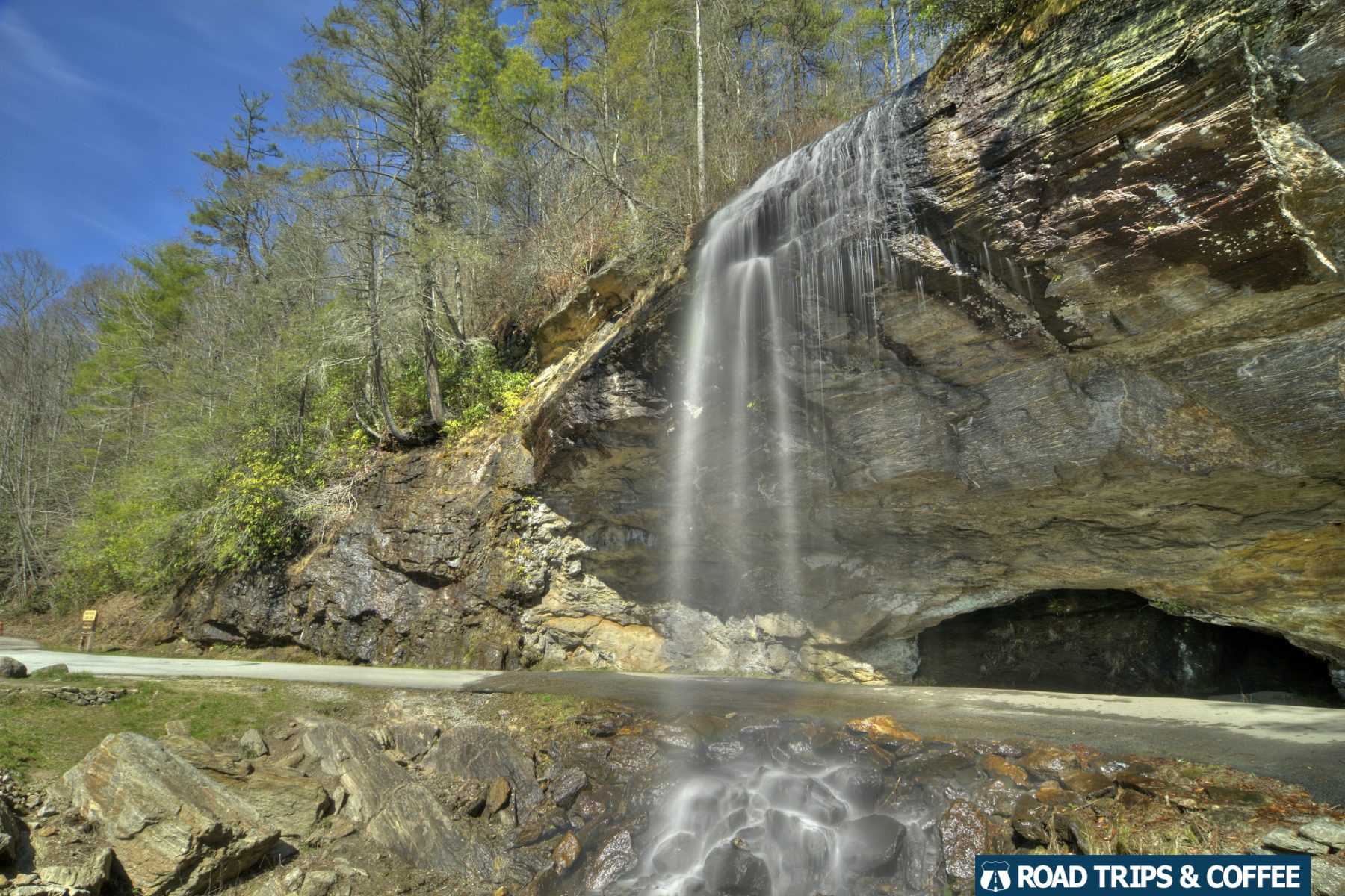 Water spills over a ledge across a narrow paved road at Bridal Veil Falls in Highlands, North Carolina