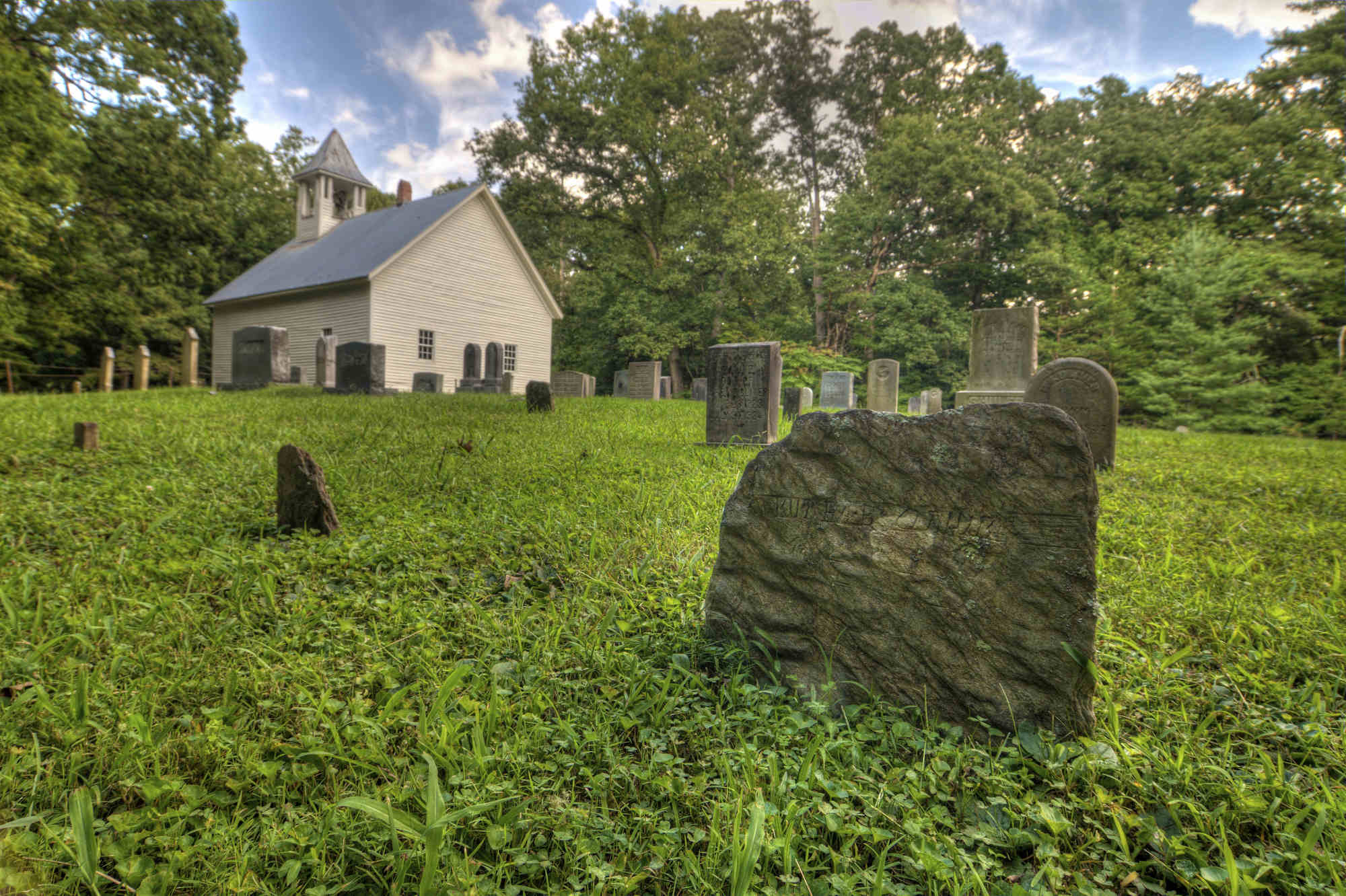 Worn tombstones mark gravesites behind the all-white Cades Cove Primitive Baptist Church in Cades Cove in Great Smoky Mountains National Park.