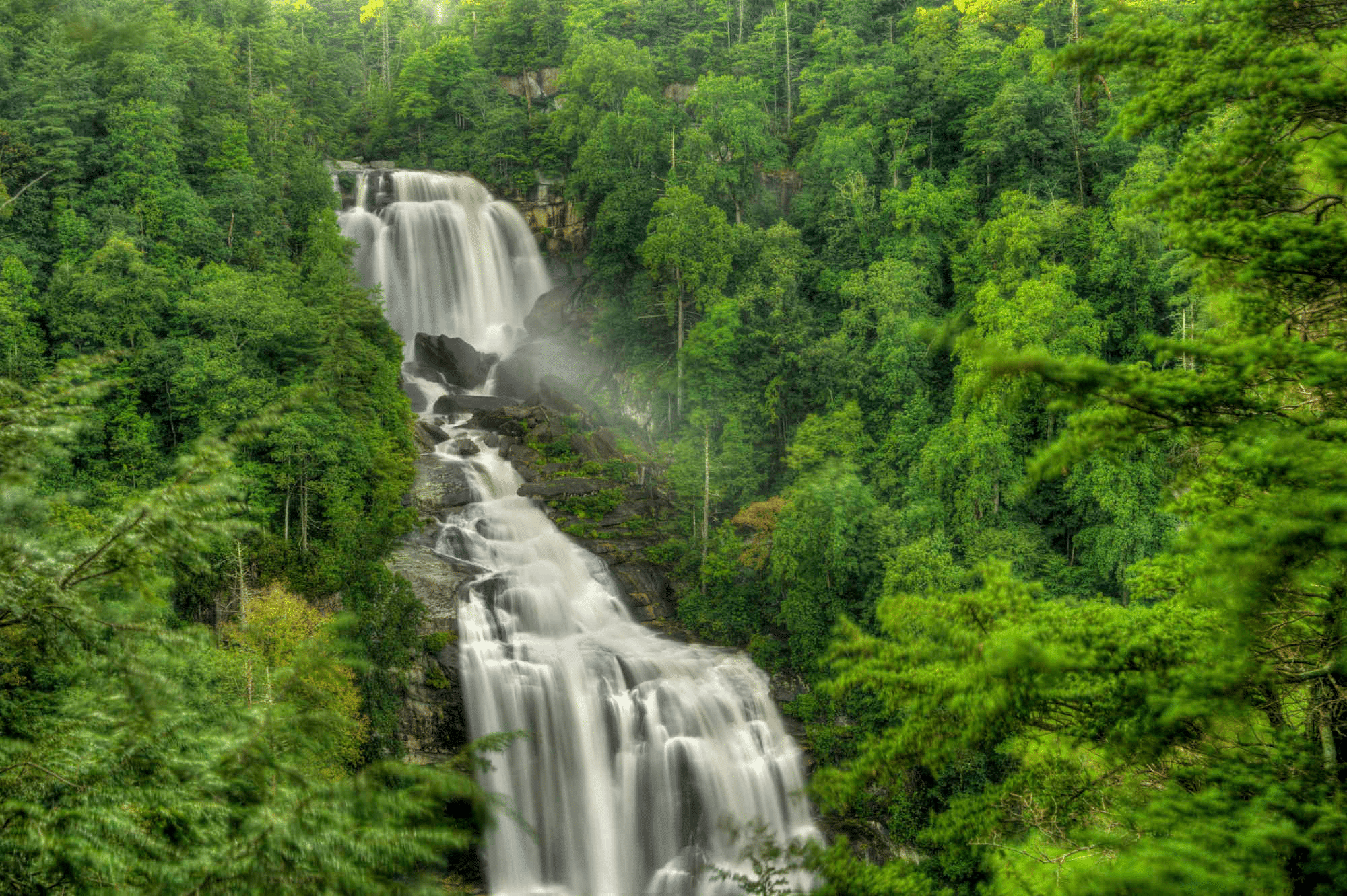 Upper Whitewater Falls is silky smooth while cascading over the rocks surrounded by lush green trees in Nantahala National Forest.